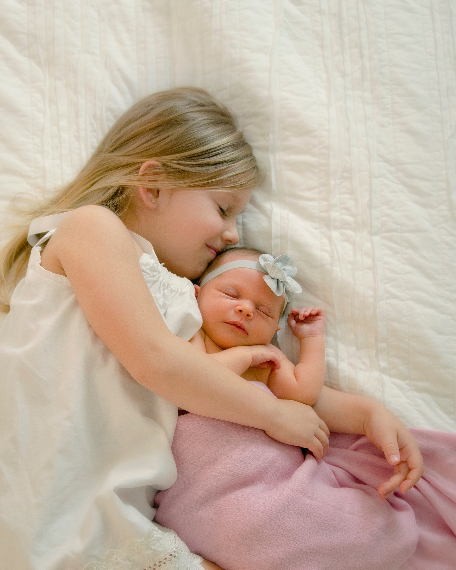Big Sister snuggling newborn baby sister in pink blanket